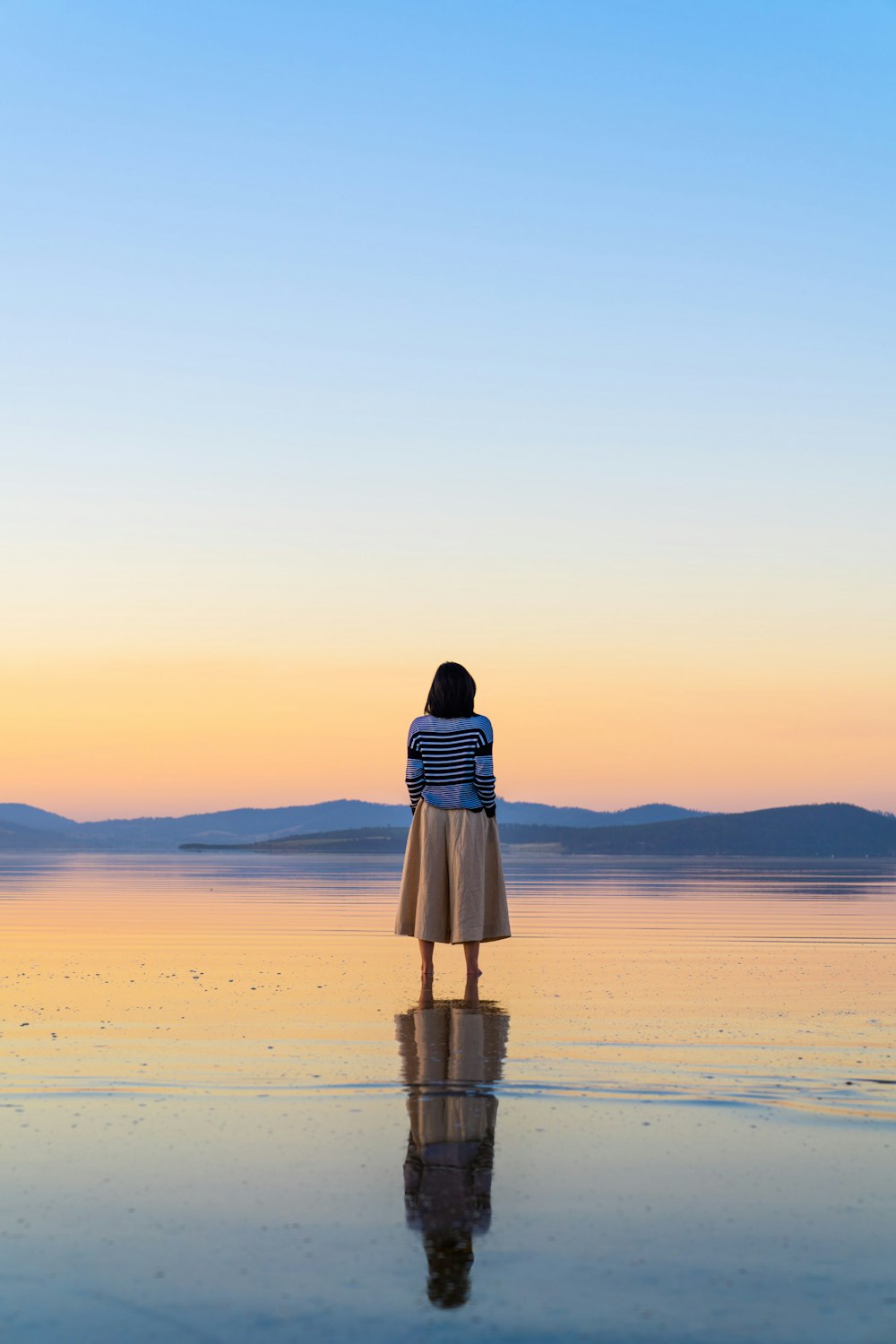 mulher no vestido preto e branco que está na praia durante o pôr do sol