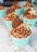 A display of assorted cupcakes in chocolate brown and champagne gold wrappers, topped with artistic frosting swirls.