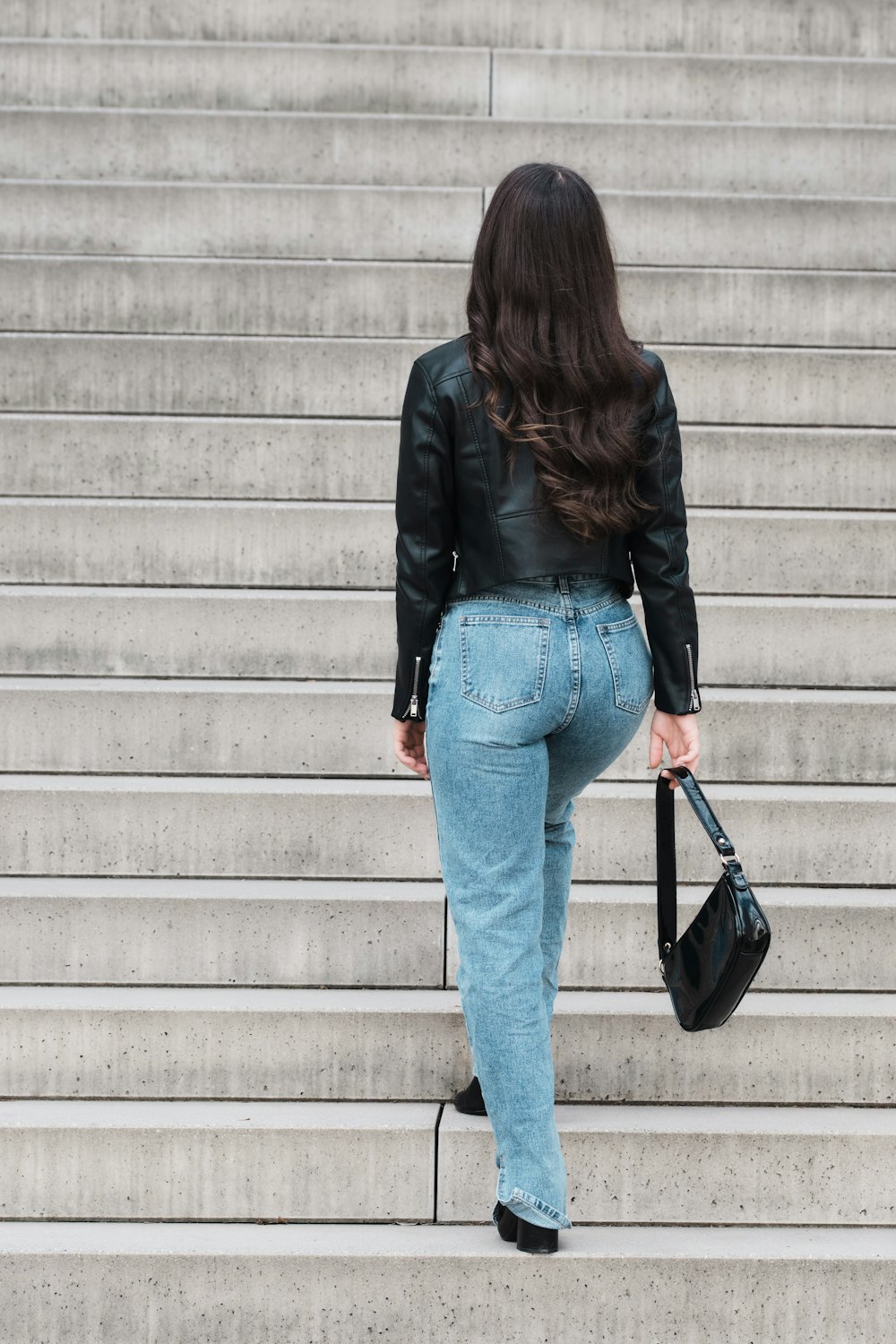 woman in black leather jacket and blue denim jeans standing on gray concrete stairs