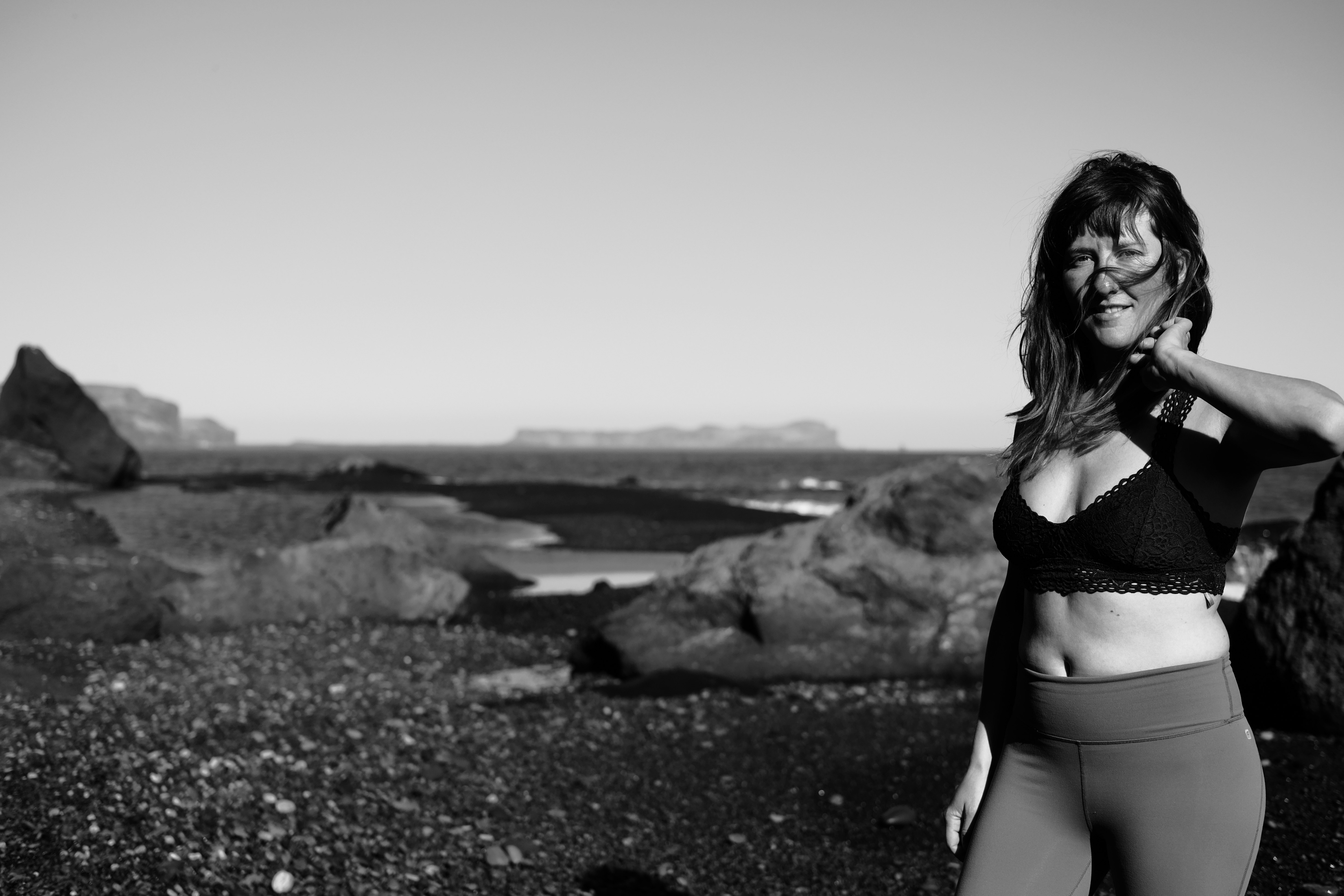 grayscale photo of woman in bikini standing on rocky shore