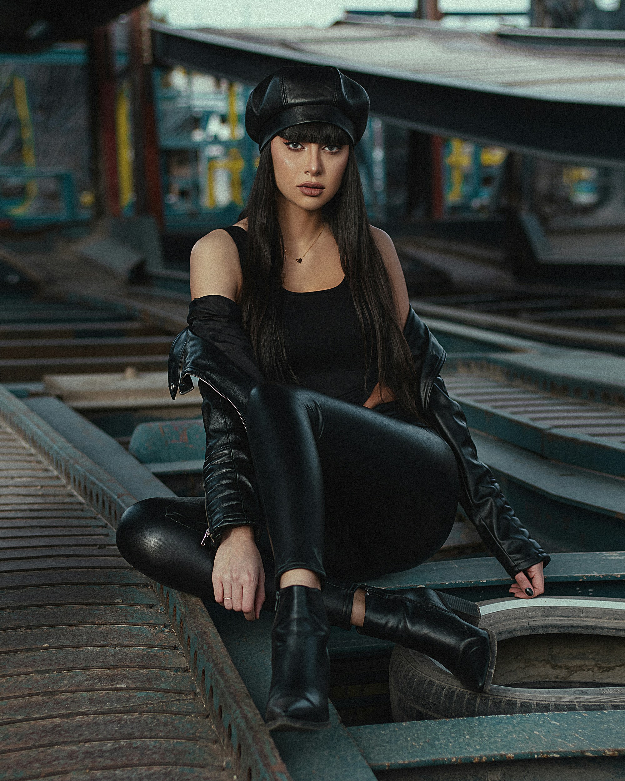 Wanita dengan jaket kulit hitam dan celana hitam duduk di rel kereta pada siang hari