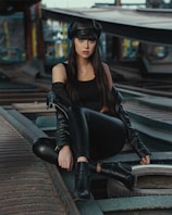 woman in black leather jacket and black pants sitting on train rail during daytime