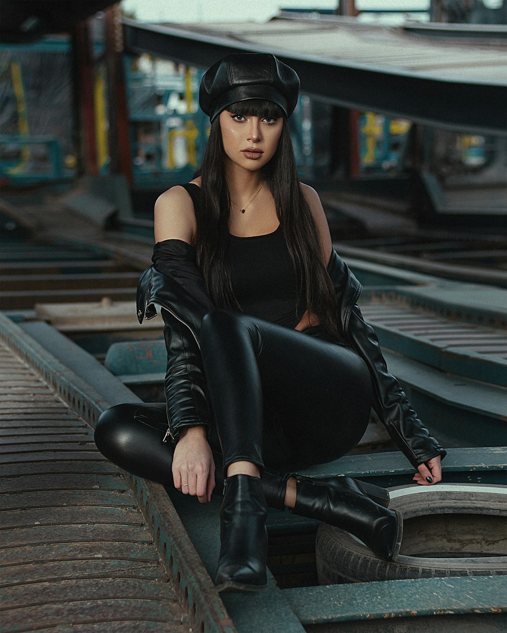 woman in black leather jacket and black pants sitting on train rail during daytime