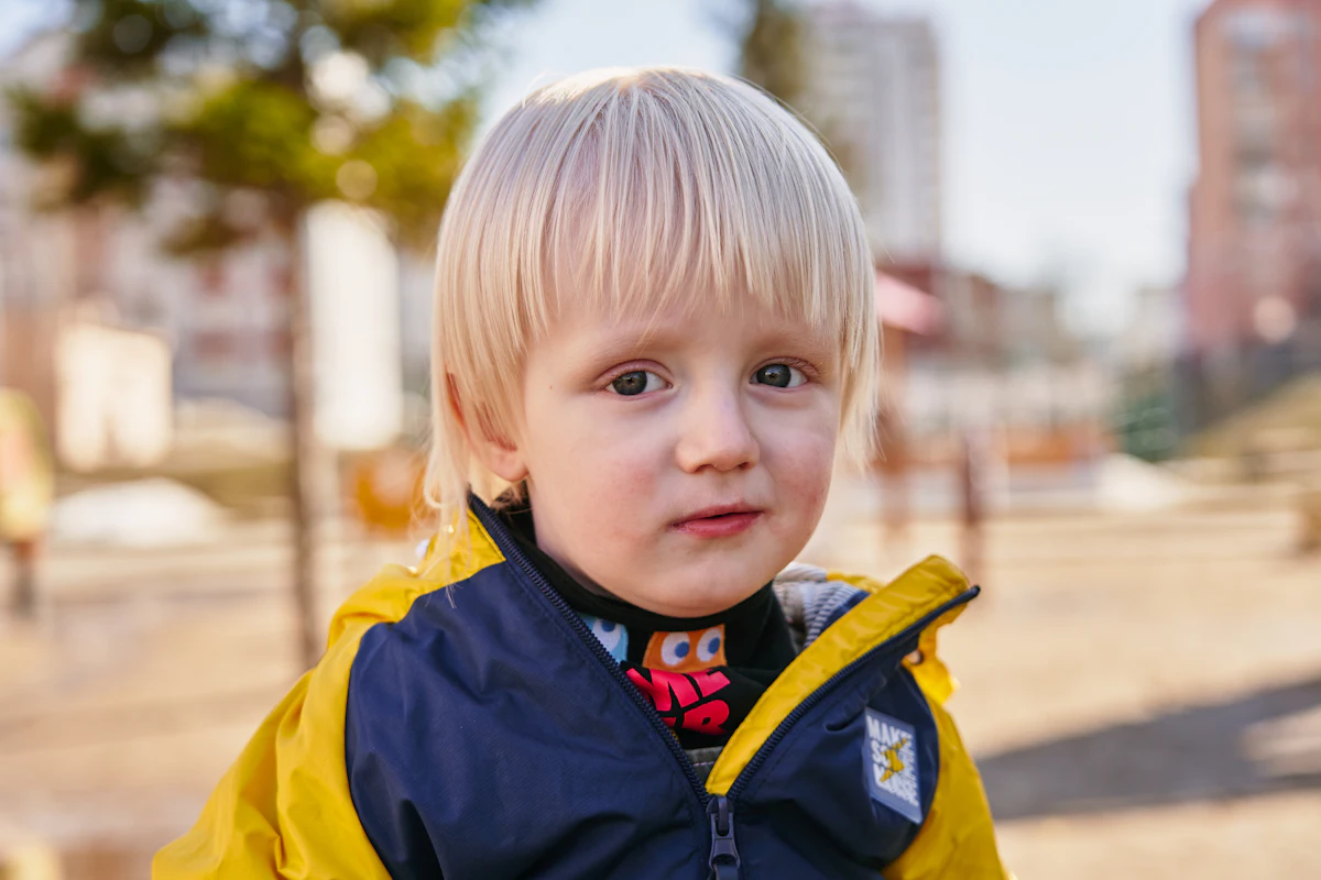 A boy in a blue and yellow zip-up jacket with a short fresh haircut.