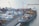 A busy shipping port with numerous stacked cargo containers is shown. Several cranes are actively loading and unloading the containers onto a large cargo ship docked at the port. The water nearby appears calm, and there are various vehicles and equipment scattered around the area, indicating a high level of activity.