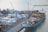 A busy shipping port with numerous stacked cargo containers is shown. Several cranes are actively loading and unloading the containers onto a large cargo ship docked at the port. The water nearby appears calm, and there are various vehicles and equipment scattered around the area, indicating a high level of activity.