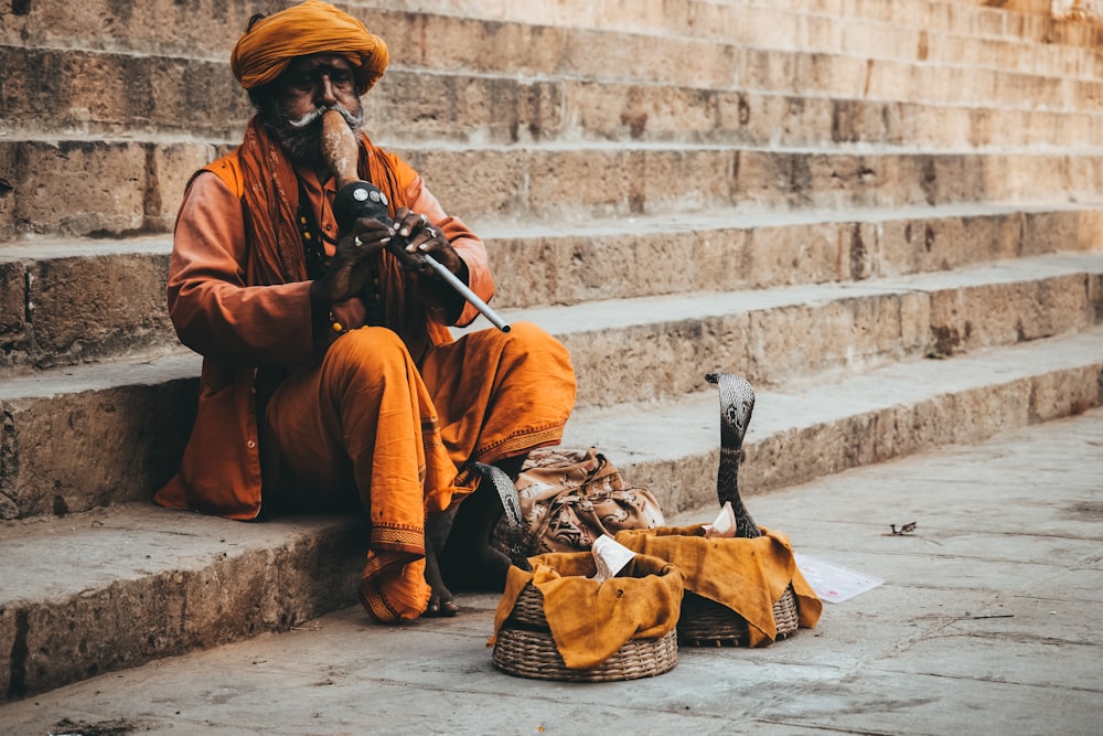 man in orange thobe sitting on concrete stairs