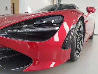 Close-up of a luxury sports car’s sleek surface under red ambient lighting highlighting flawless paint protection.