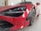 Close-up view of a luxurious red sports car with sleek design and aerodynamic features, showcased indoors in a well-lit space. The image highlights the car's front with a focus on the headlight and intricate detailing around the wheel.