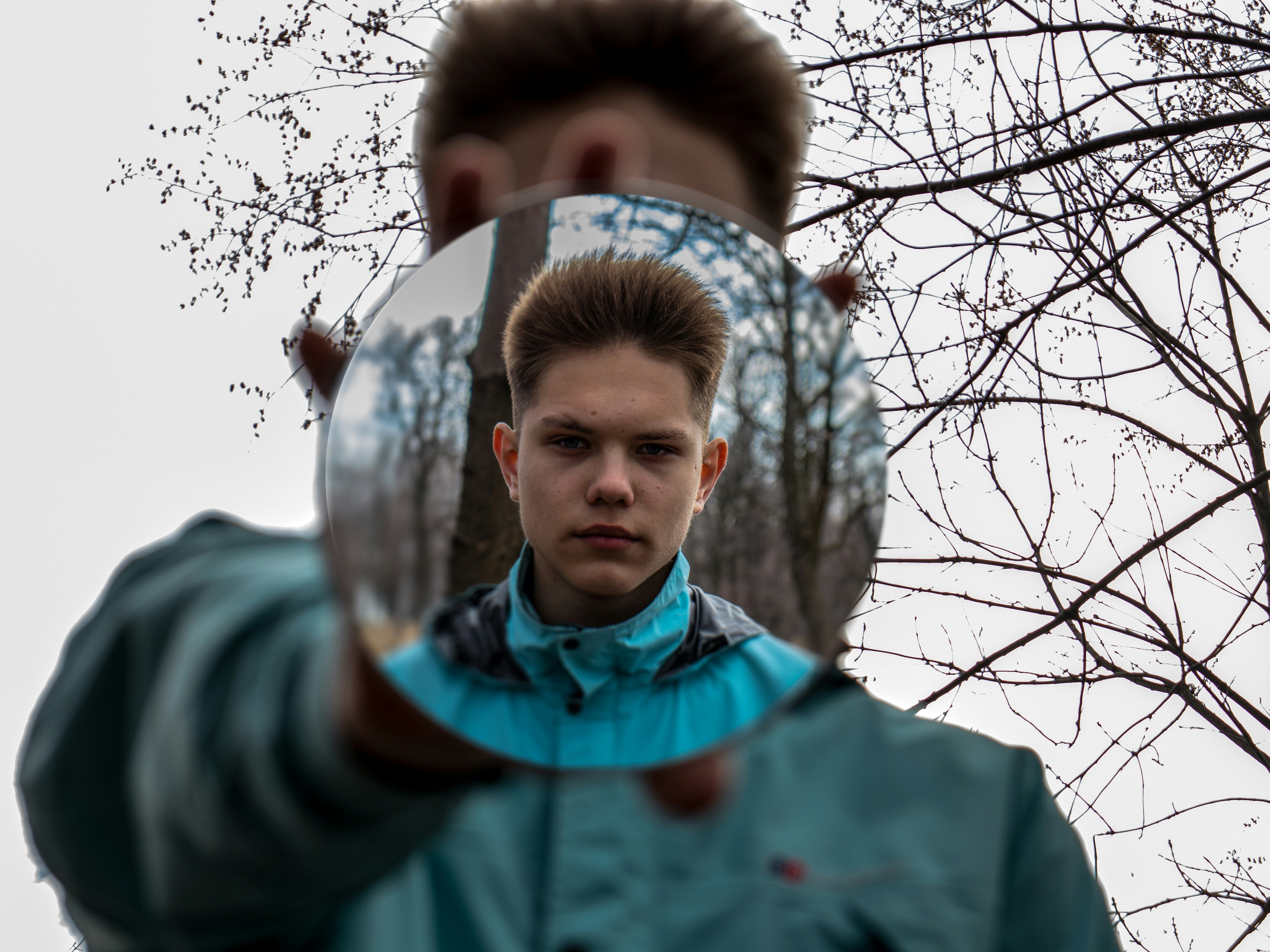 man in green and blue jacket standing near bare tree during daytime