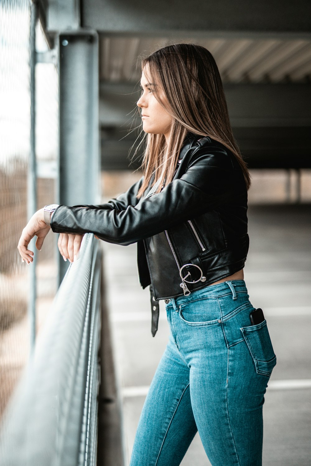 woman in black leather jacket and blue denim jeans leaning on gray metal railings