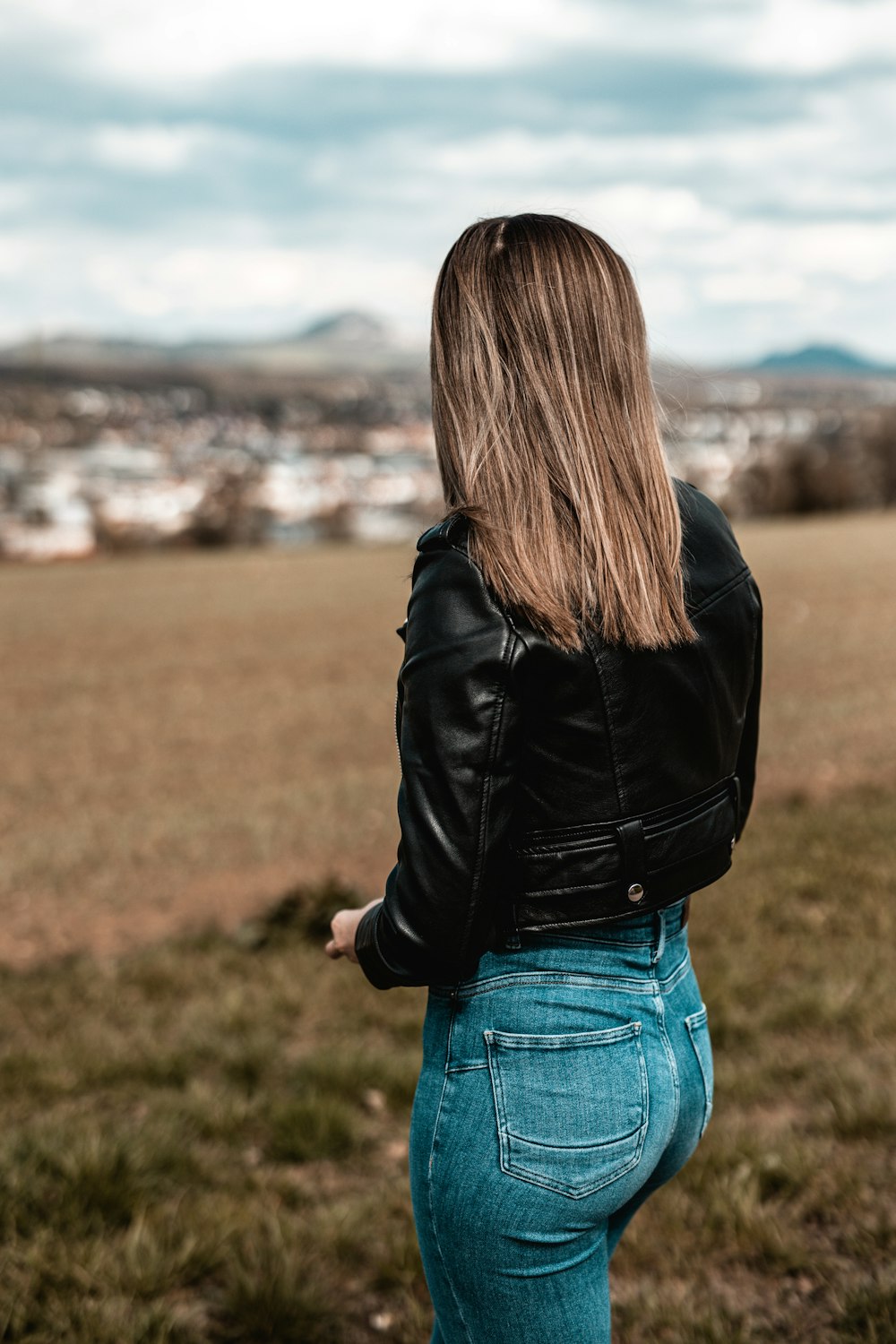 woman in black jacket and blue denim jeans standing on green grass field during daytime