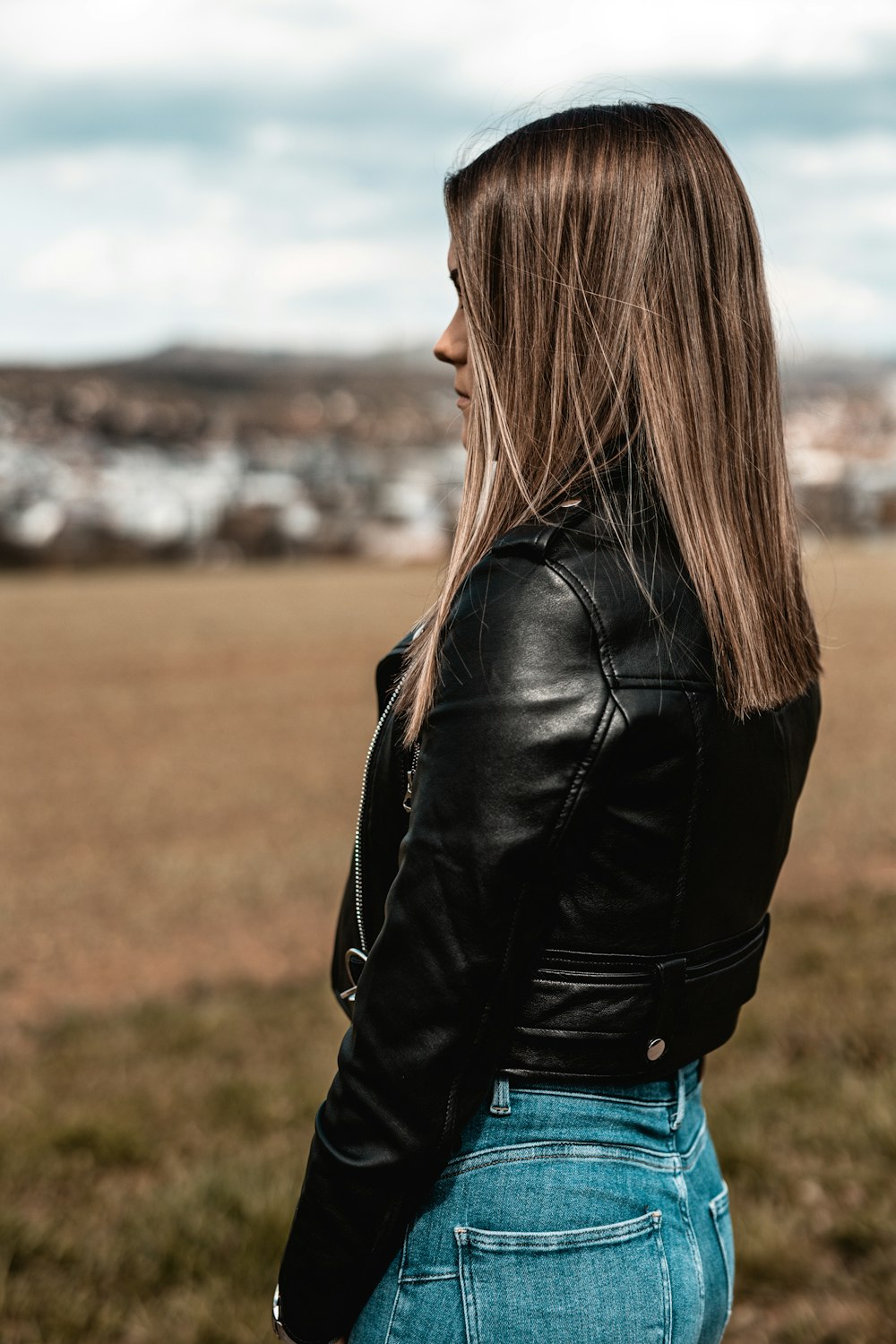 woman in black leather jacket standing on green grass field during daytime