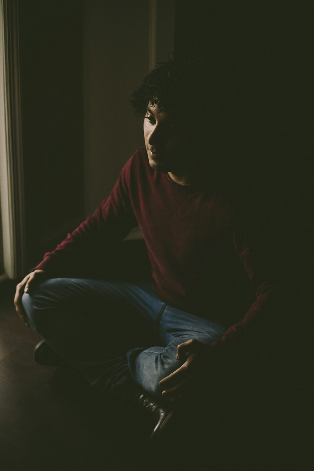 man in red long sleeve shirt and blue denim jeans sitting on floor