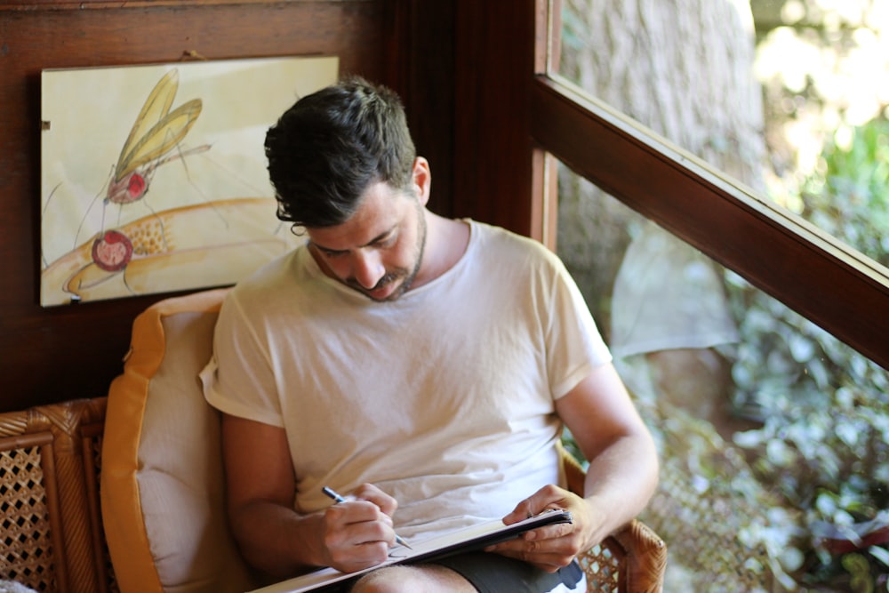 man in white crew neck t-shirt sitting on brown wooden chair