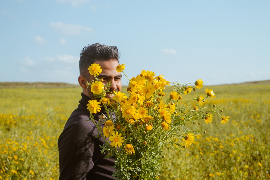 man in black jacket standing on yellow flower field during daytime