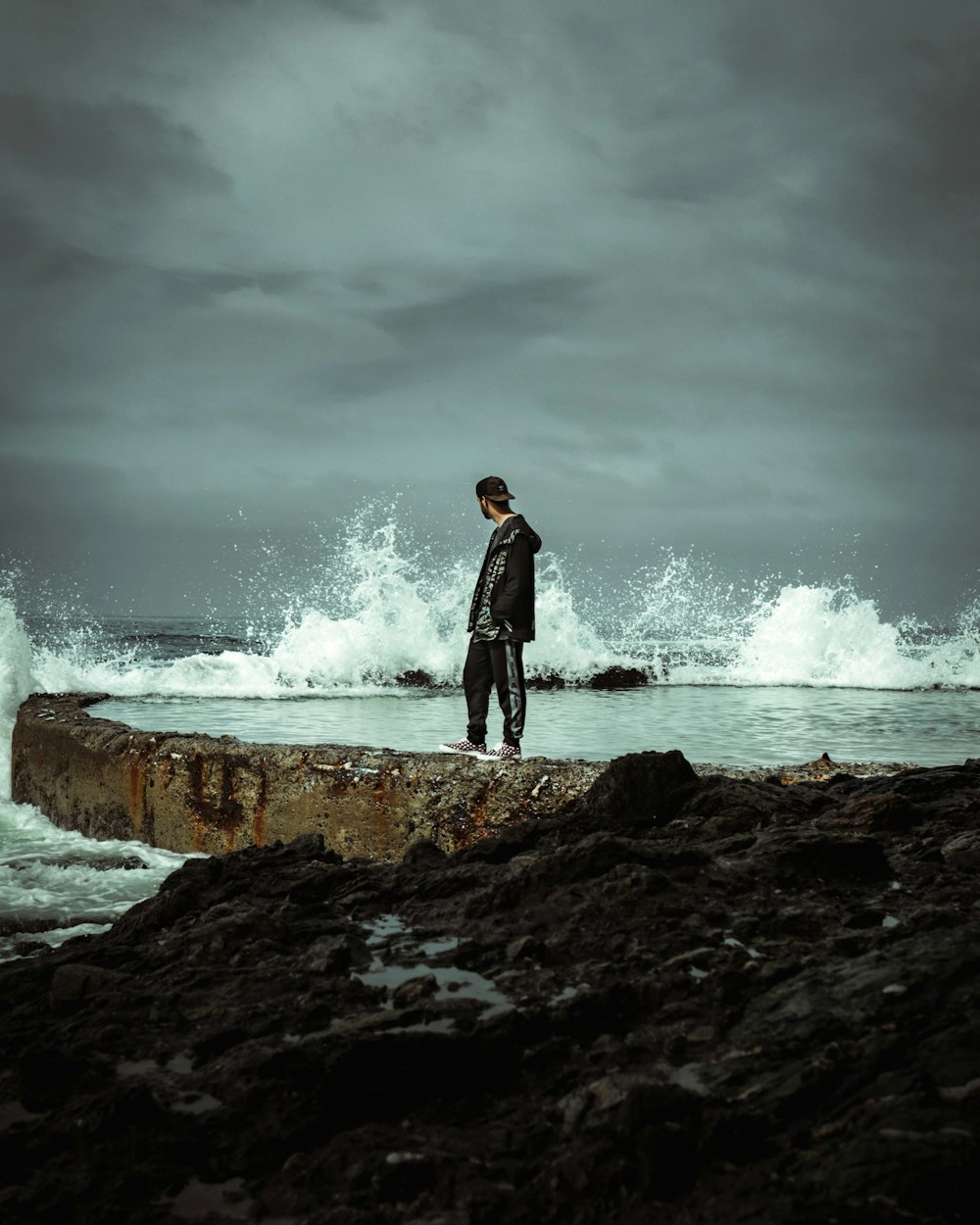 homme en veste noire debout sur un rocher près des vagues de l’océan