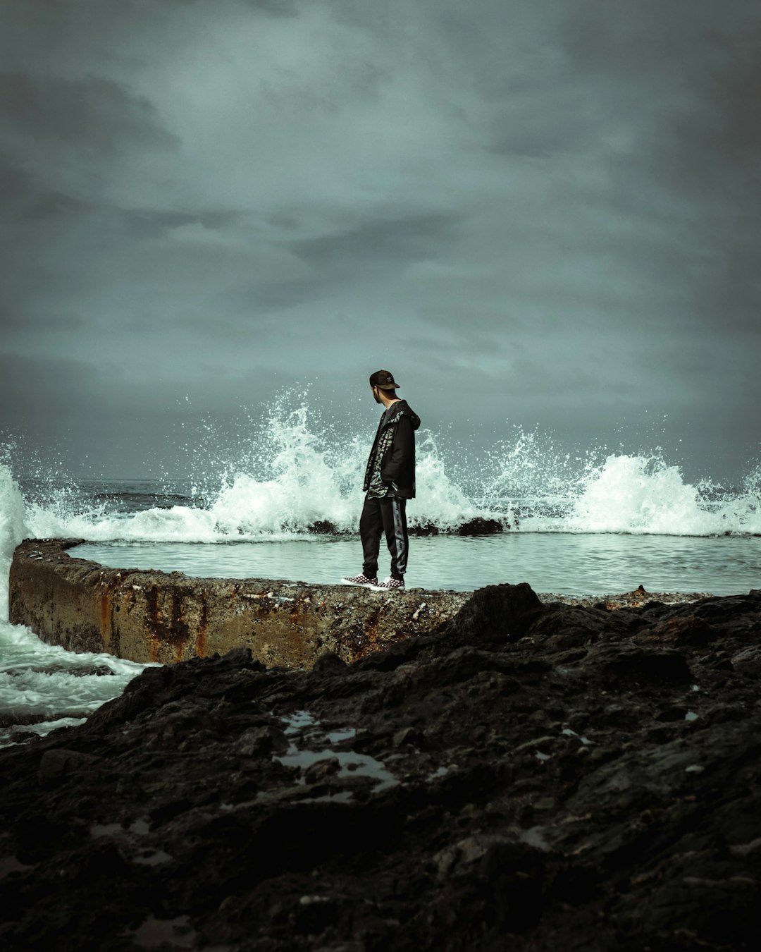 man in black jacket standing on rock near ocean waves