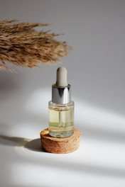 Close-up of a small amber glass bottle with a dropper, surrounded by fresh green leaves and soft sunlight.