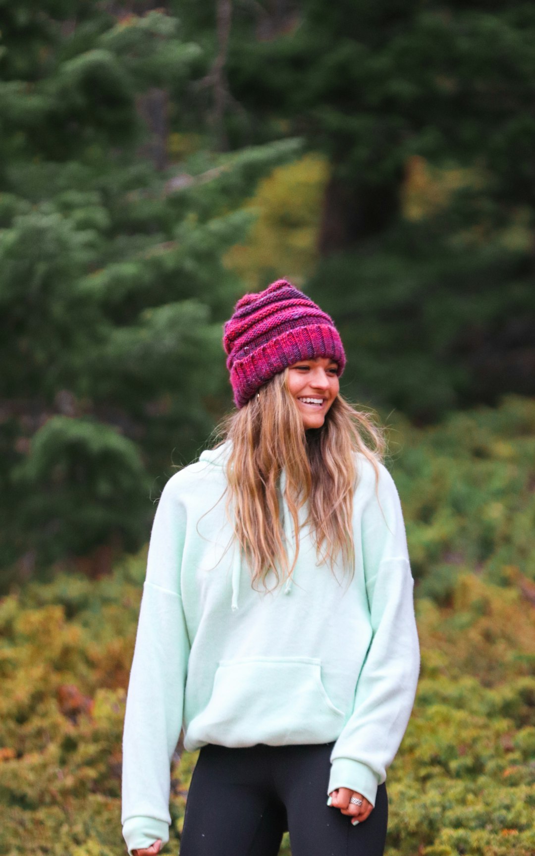 woman in white long sleeve shirt and red knit cap standing near green trees during daytime