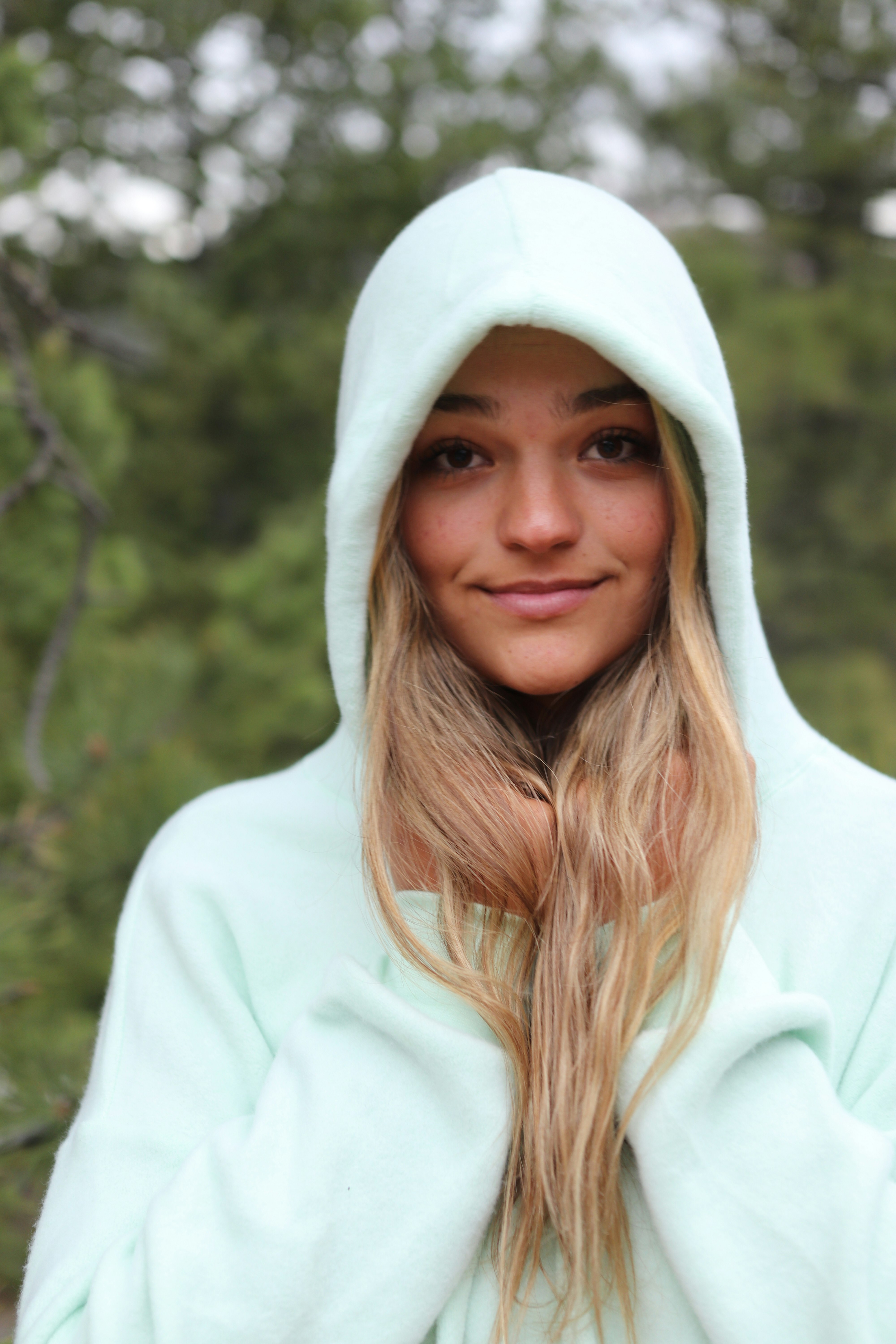 woman in white hoodie standing near green trees during daytime