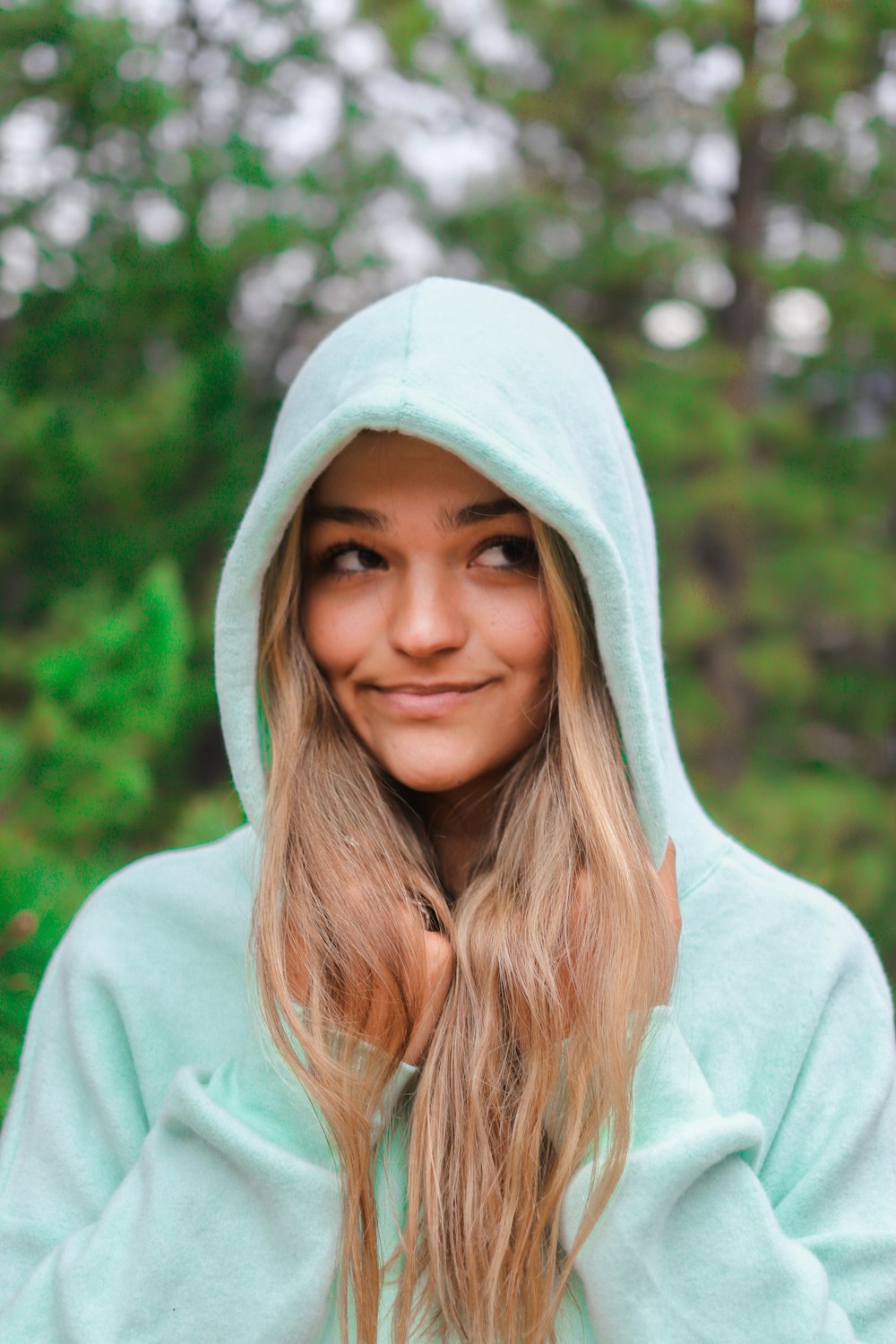 woman in white hoodie standing near green trees during daytime