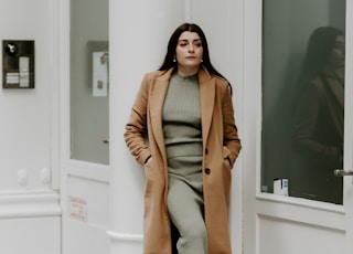 woman in brown coat and gray pants standing on white concrete staircase