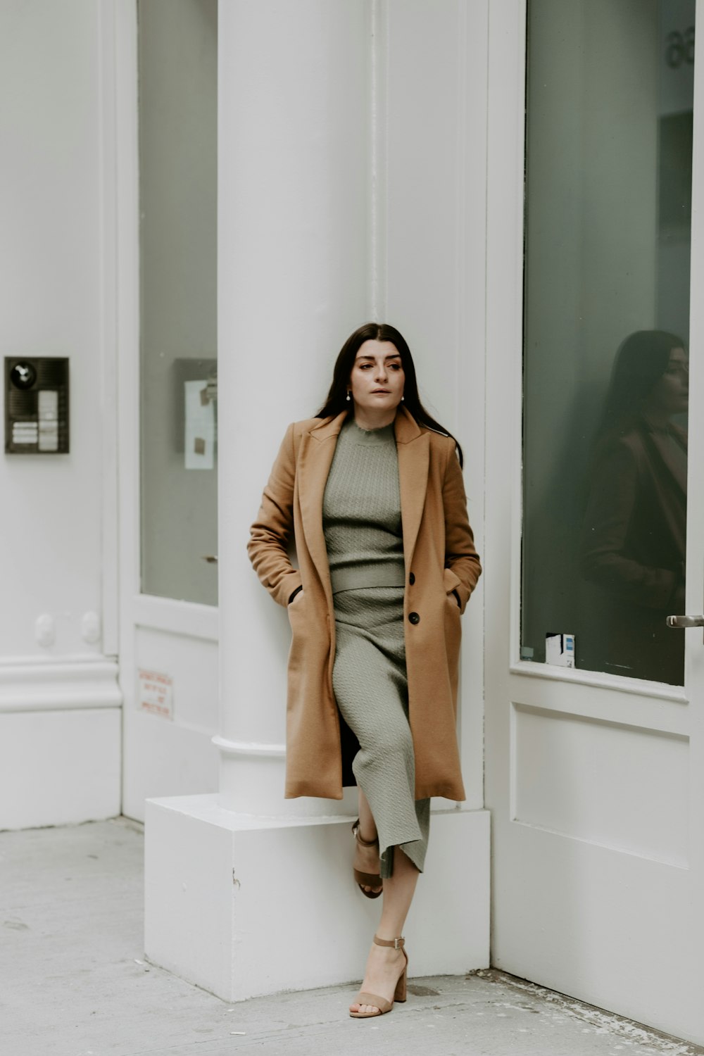 woman in brown coat and gray pants standing on white concrete staircase