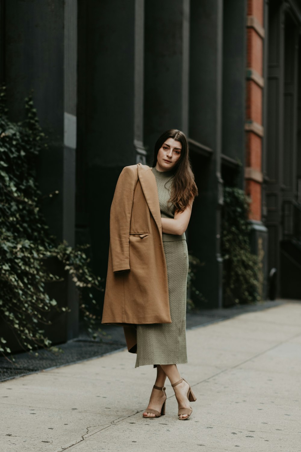 woman in brown coat standing on sidewalk during daytime