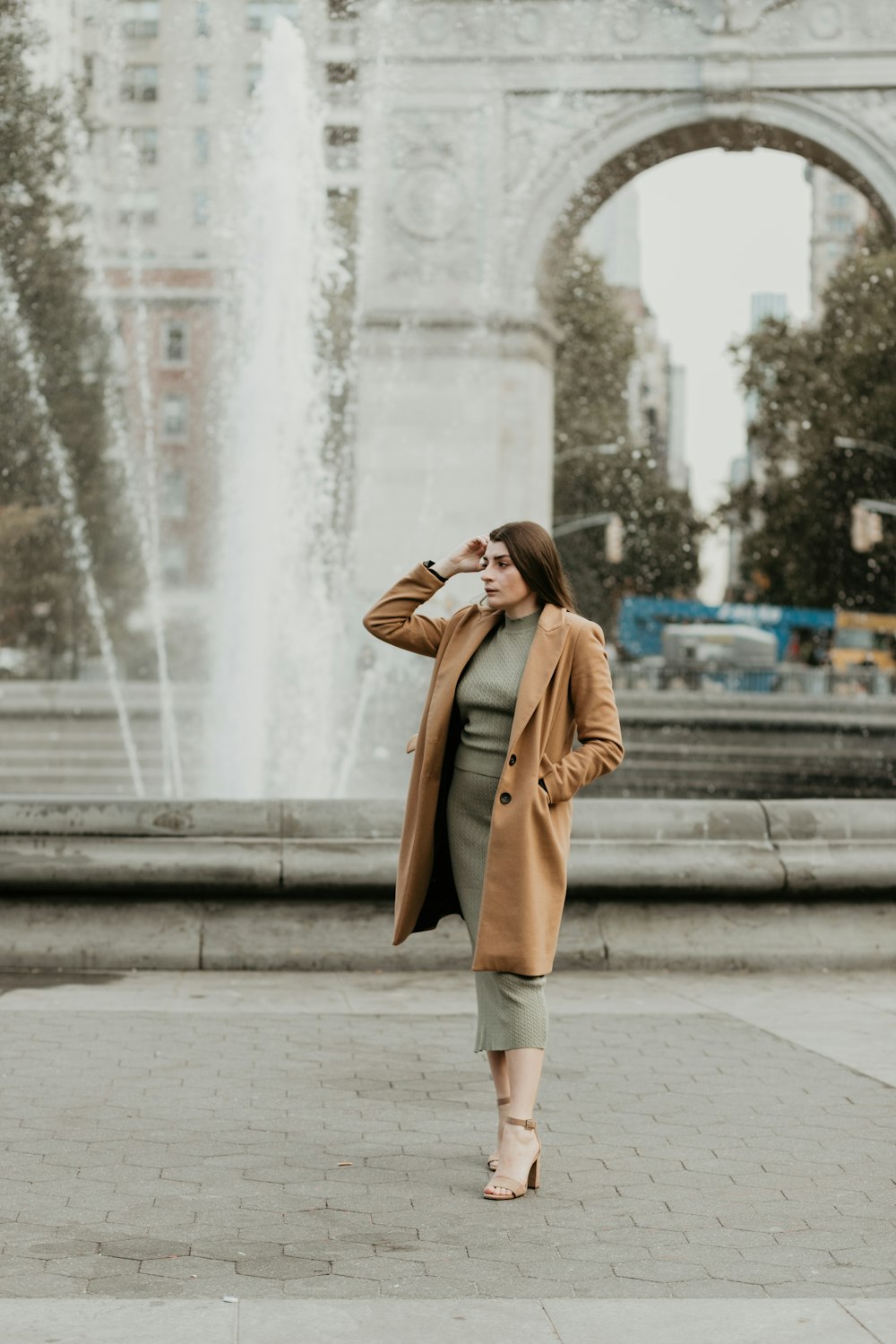 낮 동안 회색 콘크리트 바닥에 서 있는 갈색 코트를 입은 여자