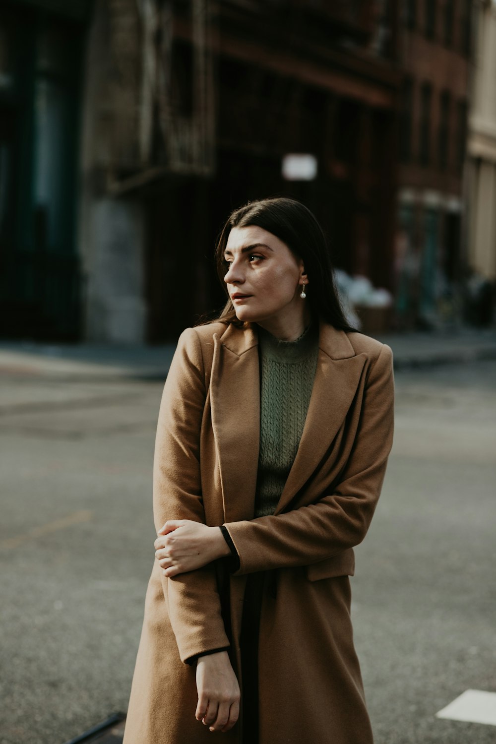 woman in brown coat standing on sidewalk during daytime