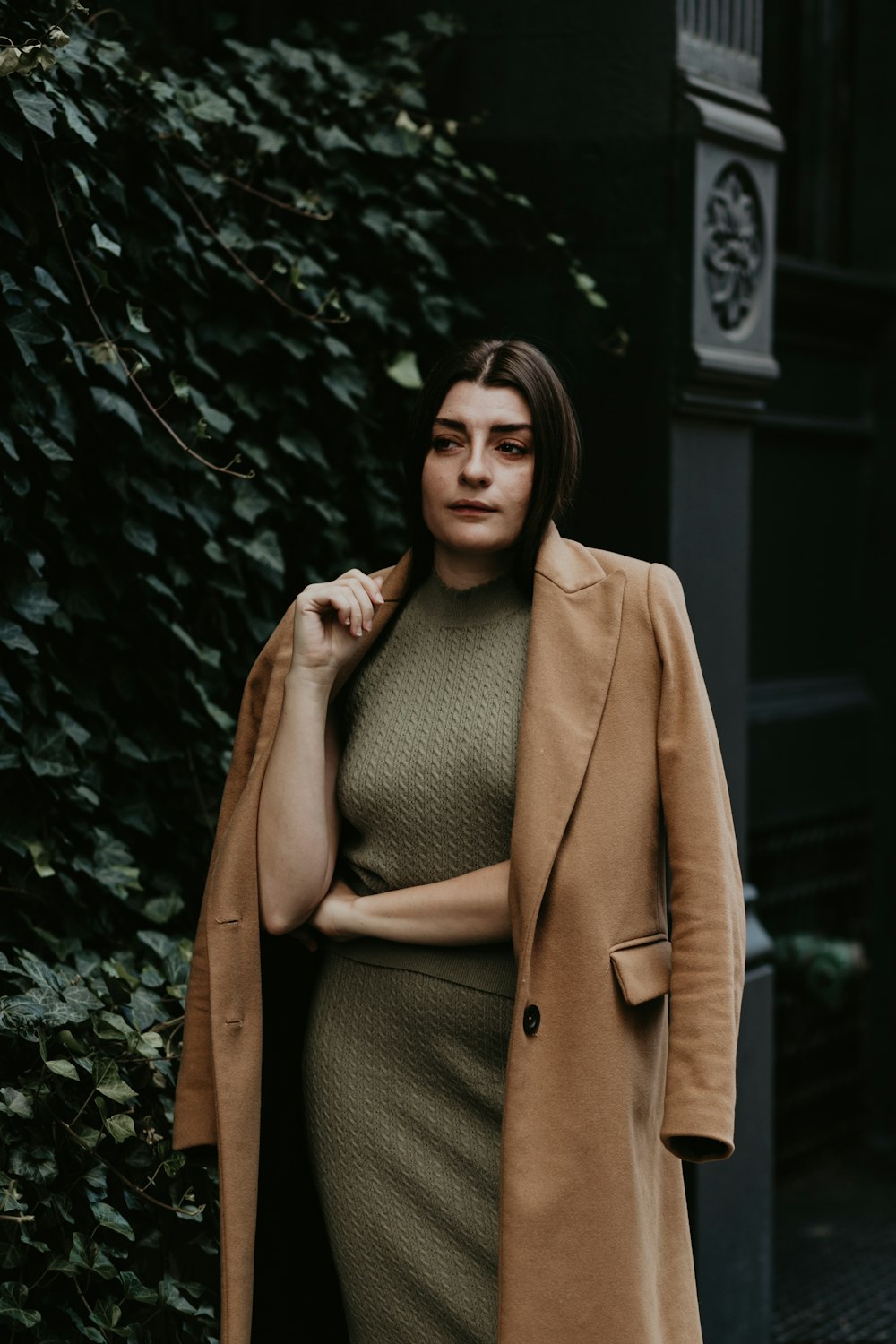 woman in brown coat standing near green plant