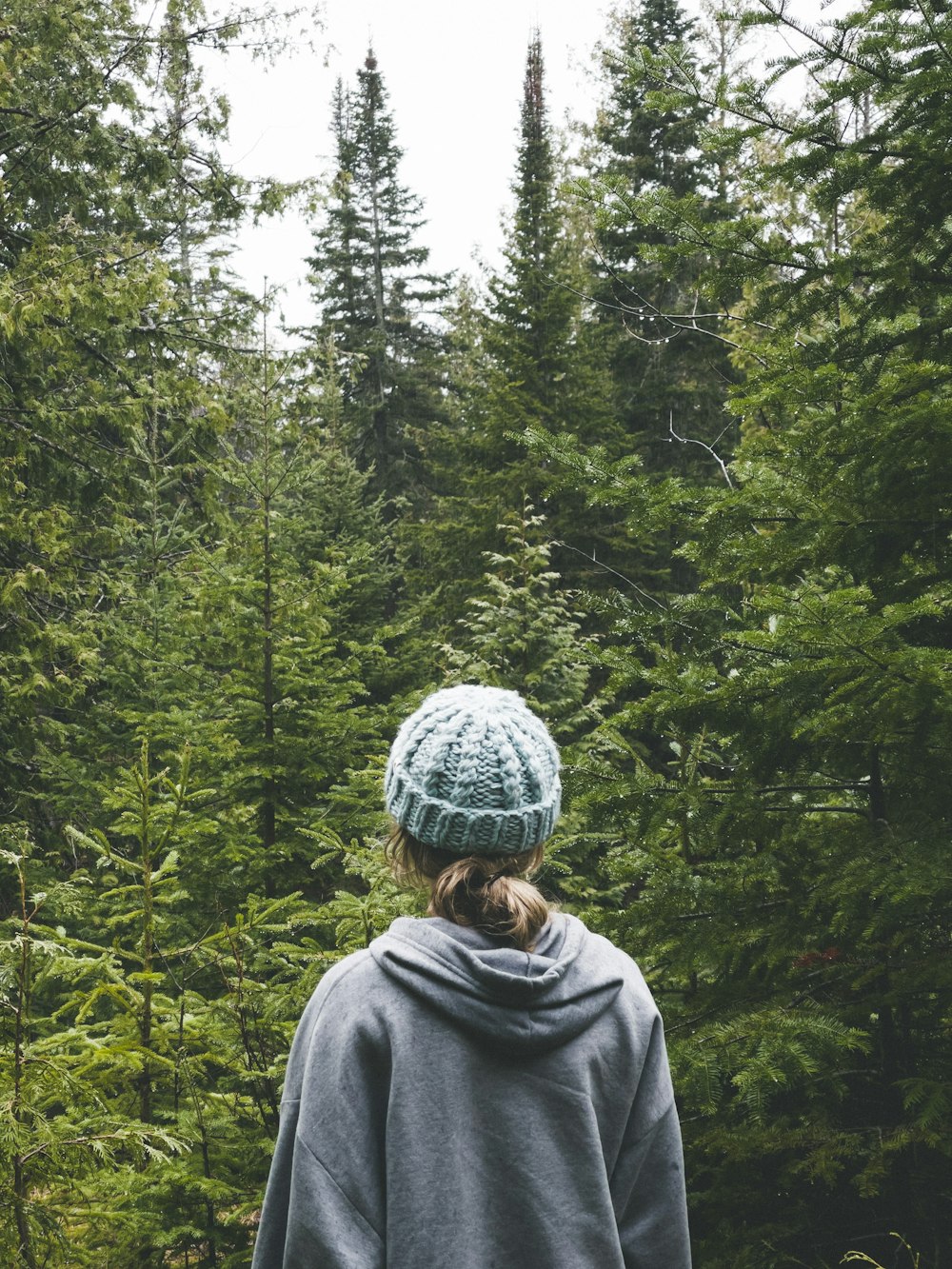 woman in gray hoodie standing in front of green trees during daytime