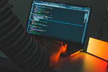 Close-up of hands coding on a laptop with glowing screen in a dark room.