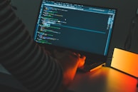 A developer coding a bespoke web application late at night, illuminated by screen light.