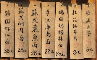 Several aged paper menus with Chinese calligraphy are displayed, each listing different dishes and their prices in yuan. The menus are attached to a wooden surface with nails.