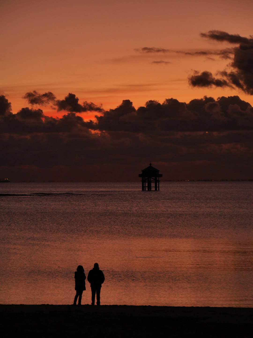 silhouette of 2 people standing near body of water during sunset