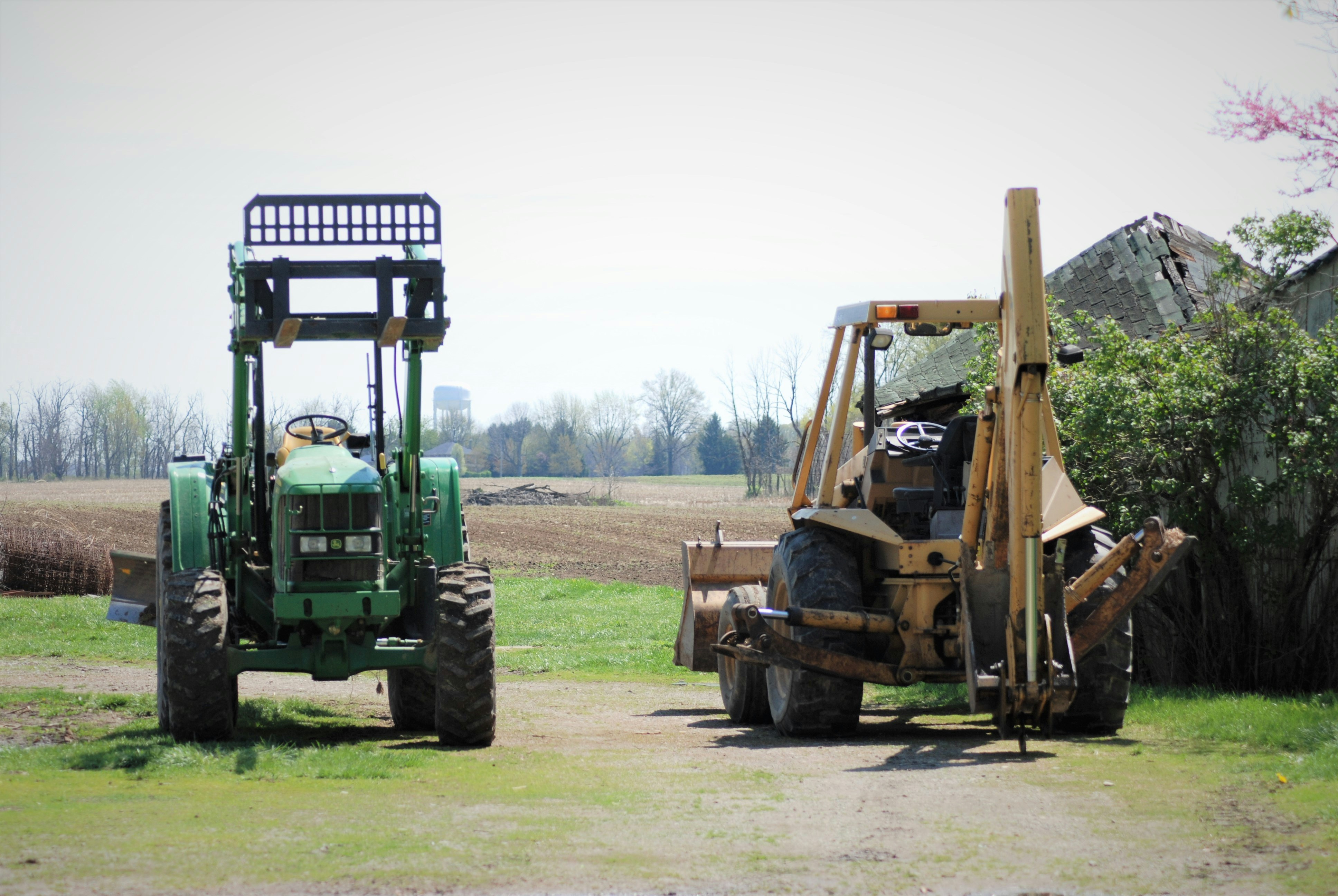 Green John Deere and yellow tractor with backhoe and front loader with collapsed barn