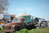 A rugged commercial truck parked beside a barn with farming equipment.