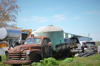 A rugged commercial truck parked beside a barn with farming equipment.