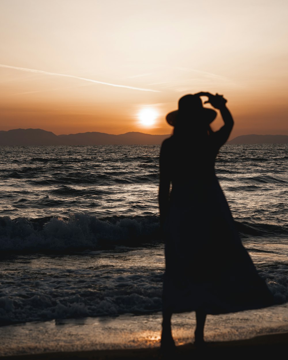 Silhouette einer Frau, die während des Sonnenuntergangs am Meeresufer steht