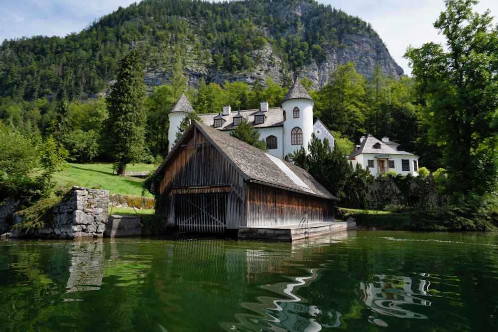 Braunes Holzhaus am grünen See in der Nähe von grünen Bäumen und Bergen tagsüber