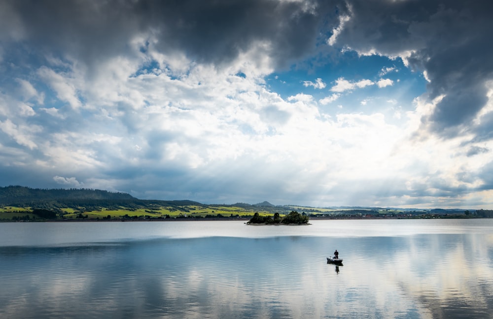 Persona que viaja en bote en el lago bajo el cielo azul y las nubes blancas durante el día