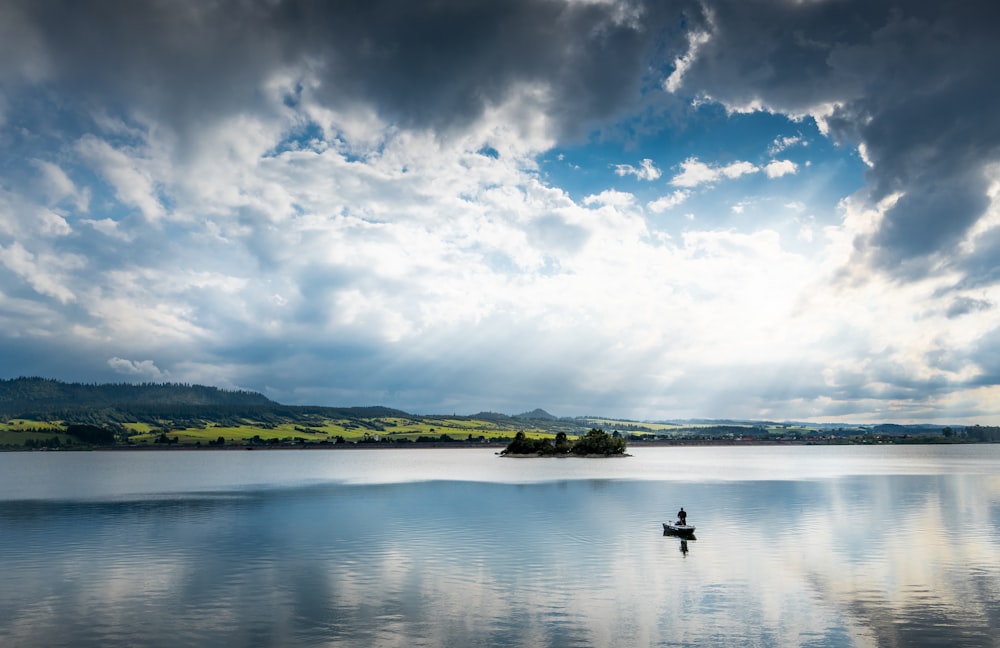 person riding on boat on lake under blue sky and white clouds during daytime