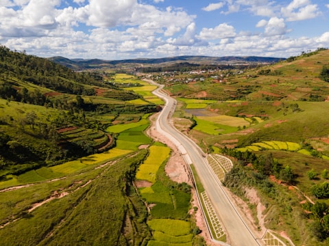 aerial view of road between green grass field under blue sky and white clouds during daytime