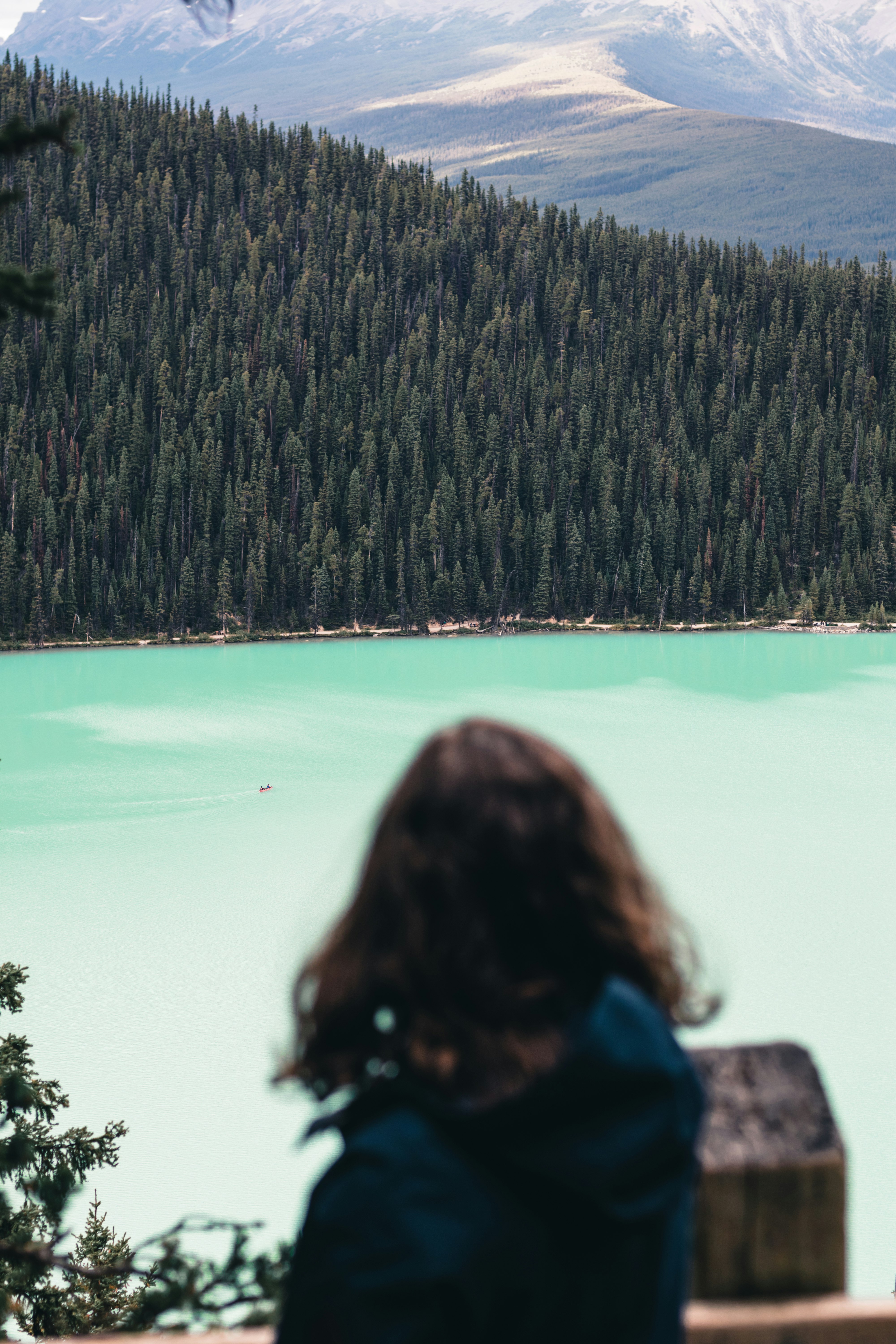 woman in blue jacket sitting on rock looking at the lake