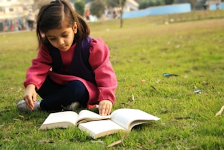 A young girl reading a book under a tree, surrounded by nature and sunlight.