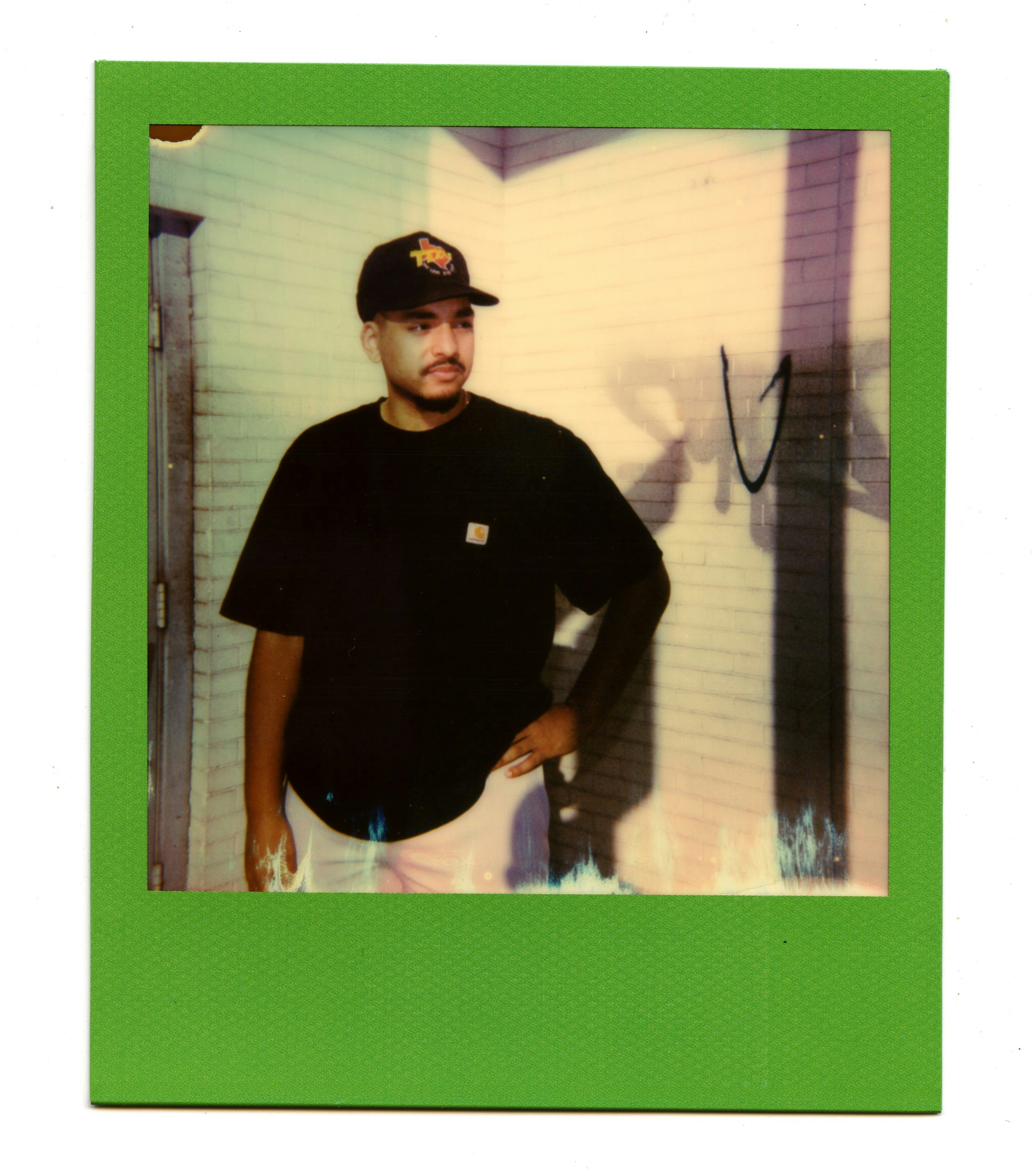 man in black crew neck t-shirt and black cap standing near green wall