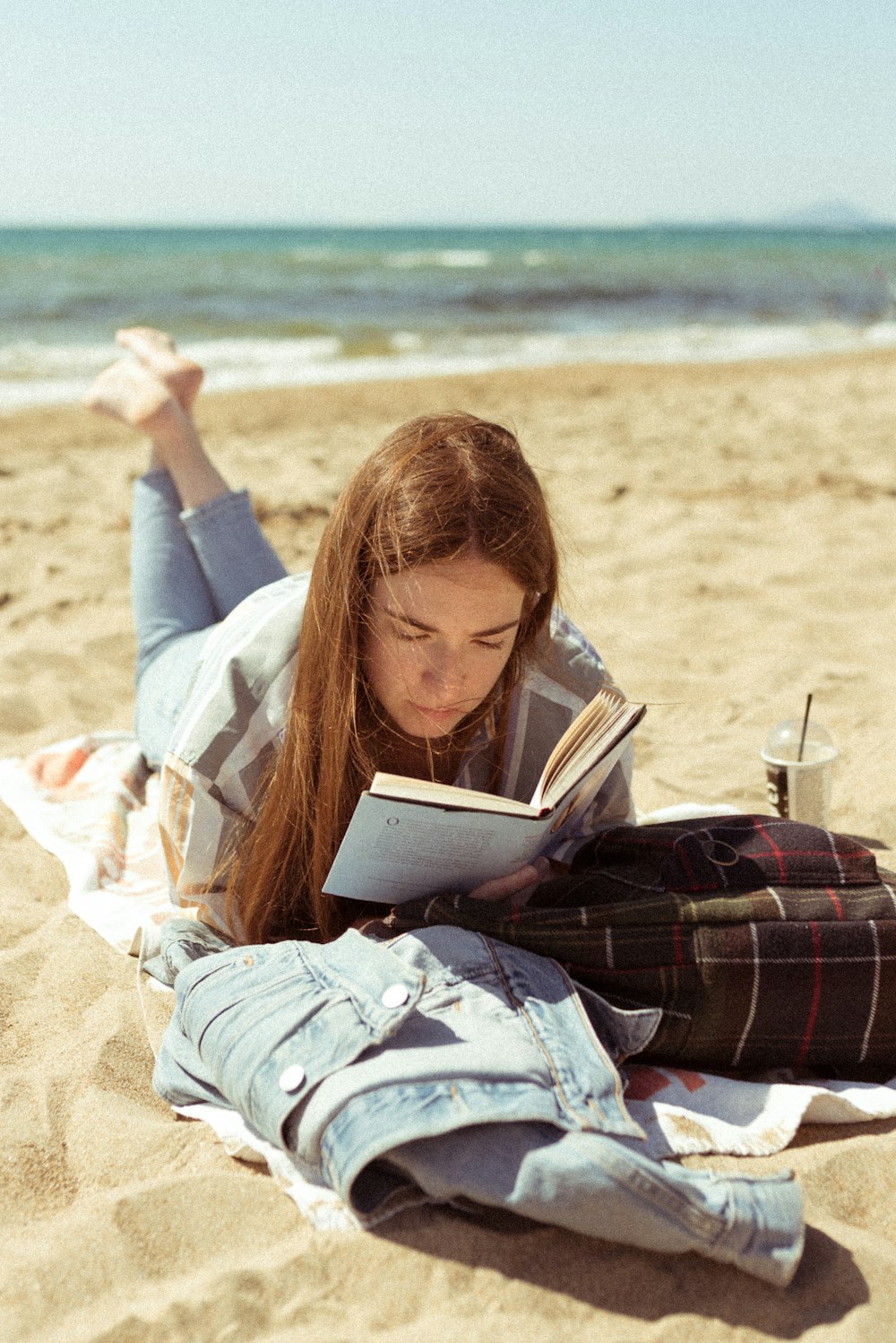 흰색 긴팔 셔츠를 입은 여자는 낮 동안 해변에서 책을 읽고 있다