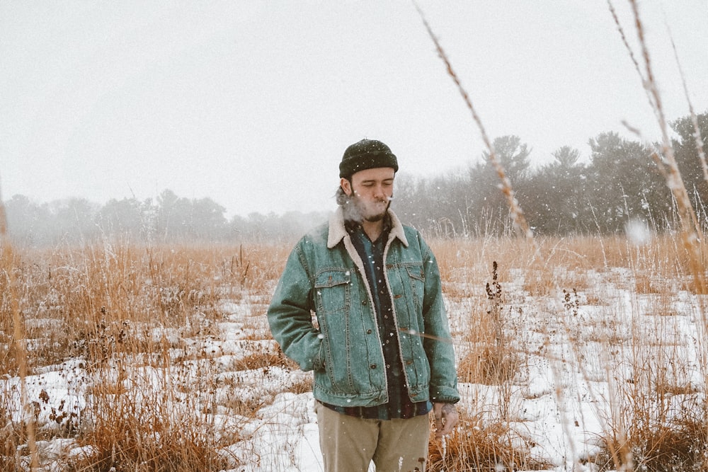 homem na jaqueta verde em pé no campo de grama marrom durante o dia